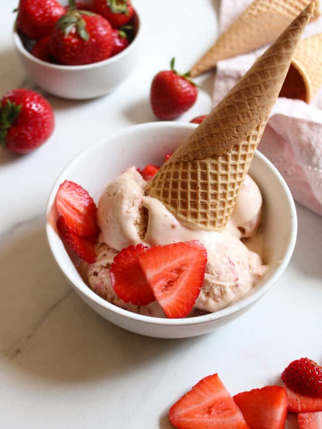 Close up on strawberry ice cream in a bowl with an ice cream cone and fresh strawberries on top.