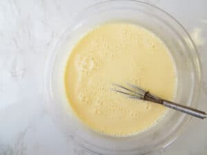 Eggs custard whisked with warm milk in a bowl with a whisk.