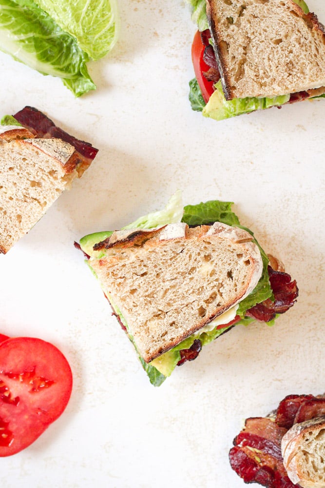 Overhead image of blt sandwiches on a table with tomatoes and lettuce.