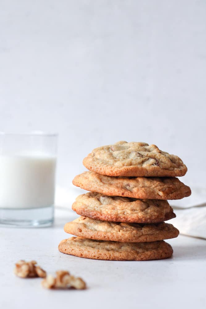Chocolate chip cookies stacked with nuts on a table and a glass of milk.