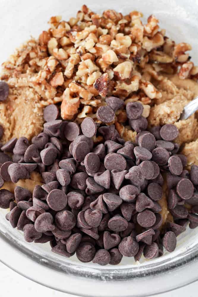 Close up on cookie dough with chocolate chips and chopped walnuts in a bowl with a spoon.
