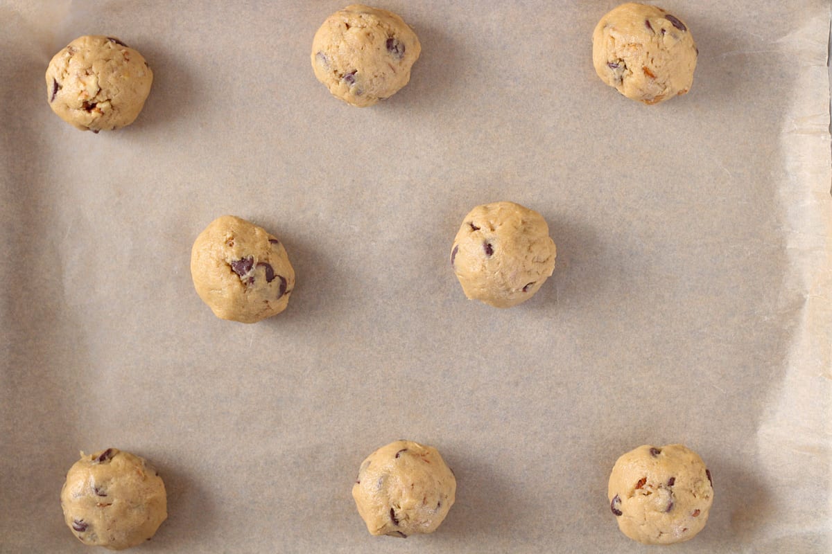 Chocolate chip cookie dough balls on a sheet pan.
