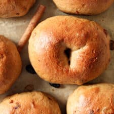 Top view of baked bagels on a sheet pan with raisins and cinnamon sticks.