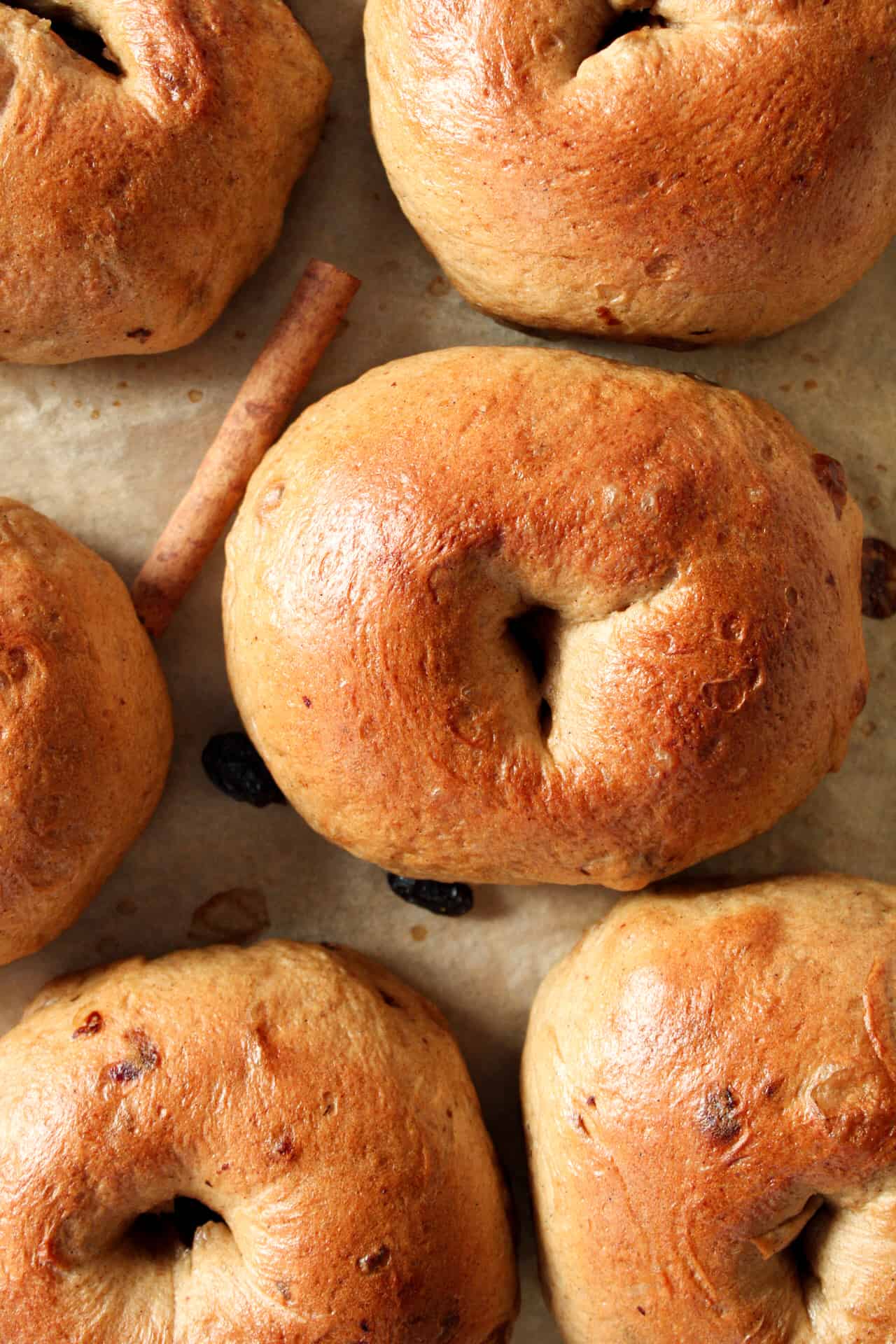 Top view of baked bagels on a sheet pan with raisins and cinnamon sticks.