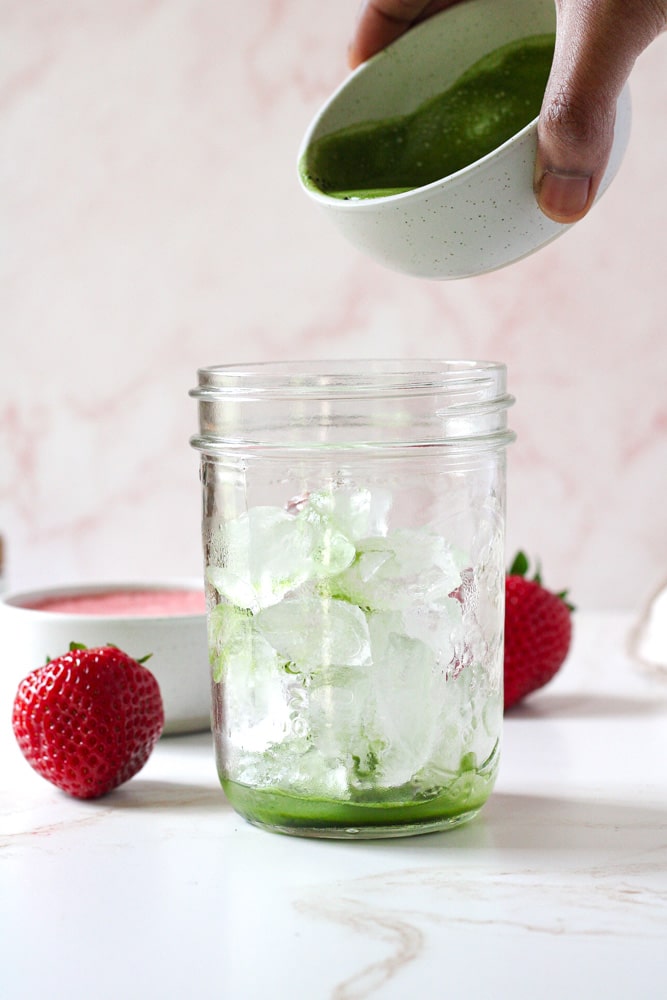 Side image of ice in a mason jar with a woman's hand holding a bowl of matcha paste.