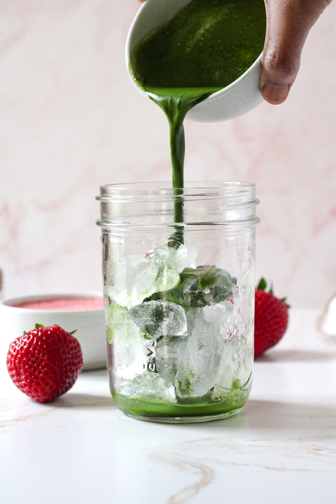 Pouring image of matcha into a mason jar with ice.