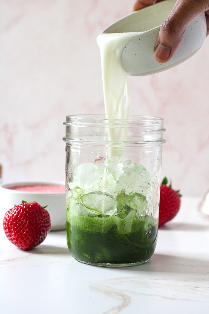 Pouring image of milk into mason jar with matcha and ice.