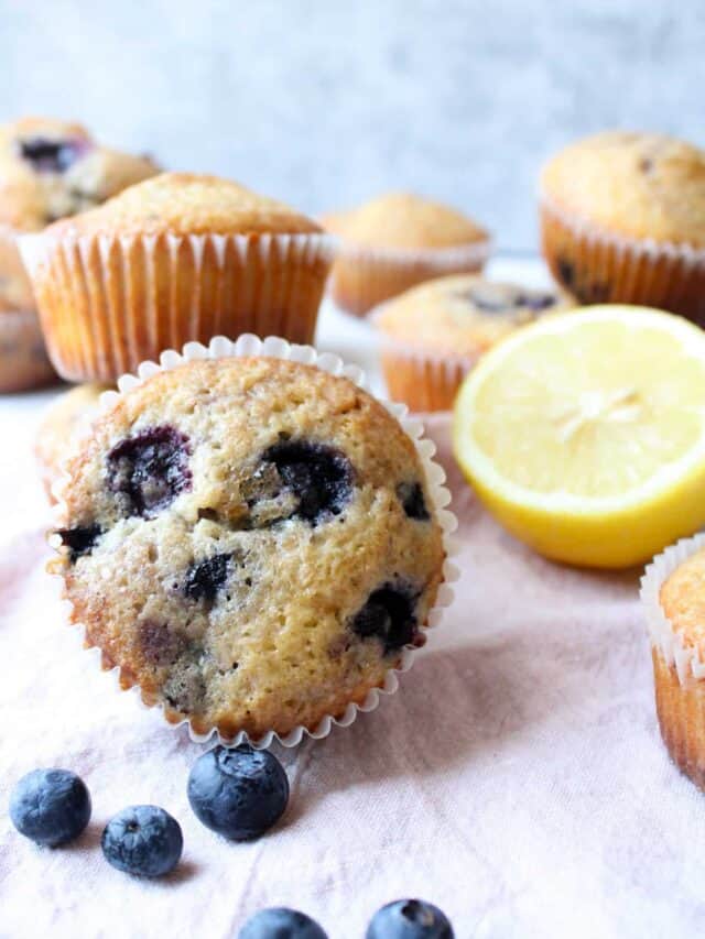 Close up on a lemon blueberry muffin with blueberries and lemon half in background.
