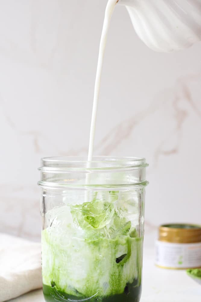 Side view of milk pouring into mason jar with matcha and ice.