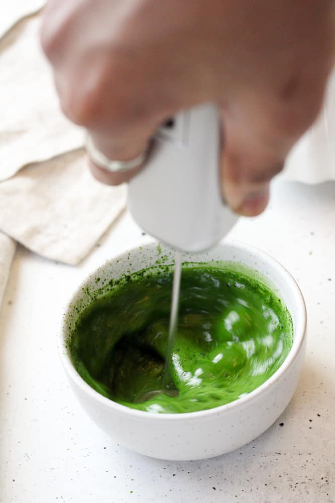 Woman whisking matcha powder and water with an electric whisk.