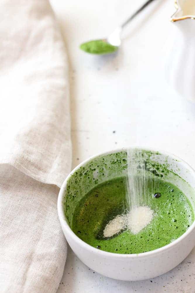 Side view of pouring sugar into small bowl with matcha paste.