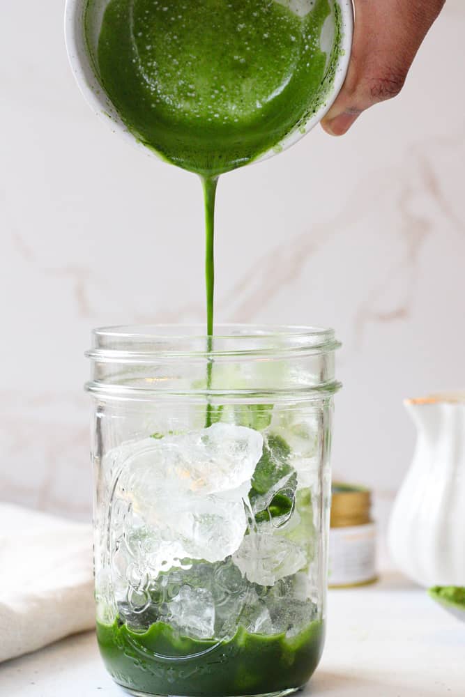 Side view of matcha mixture poured into mason jar with ice.