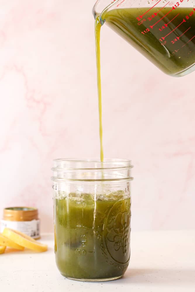 Side view of pouring matcha lemonade over ice in a mason jar.