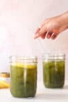 Matcha lemonade in mason jars with ice. Woman holding glass straw in background.