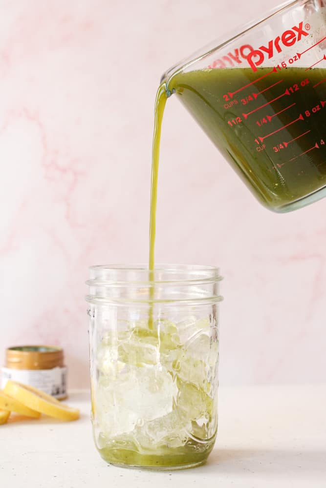 Woman pouring matcha lemonade over ice in a mason jar. 