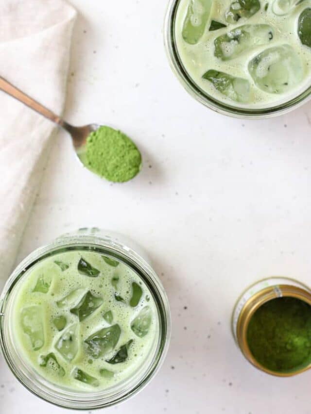 Overhead view of oat milk matcha lattes in a mason jars with a spoon of matcha powder on the table near by.