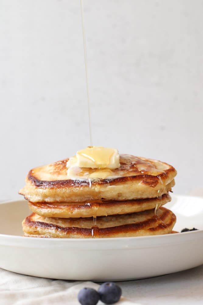 Stack of buttermilk pancakes with maple syrup drizzled over them.