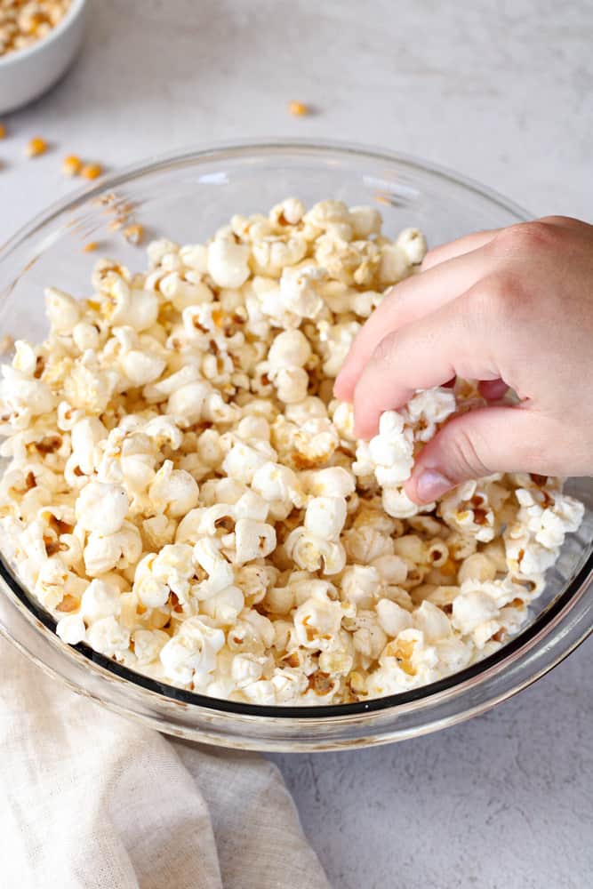 Boy's hand grabbing parmesan cheese popcorn from a bowl. 