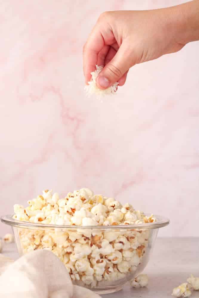 Boy's hand sprinkling parmesan cheese on a bowl of popcorn.