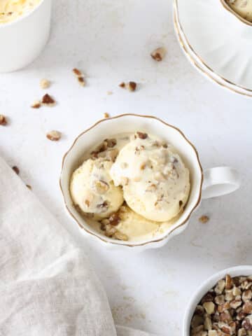 Black walnut ice cream in a tea cup with chopped nuts on top.