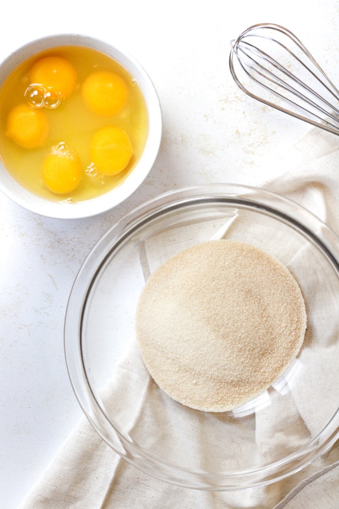 Sugar in a large bowl next to a bowl of eggs. 