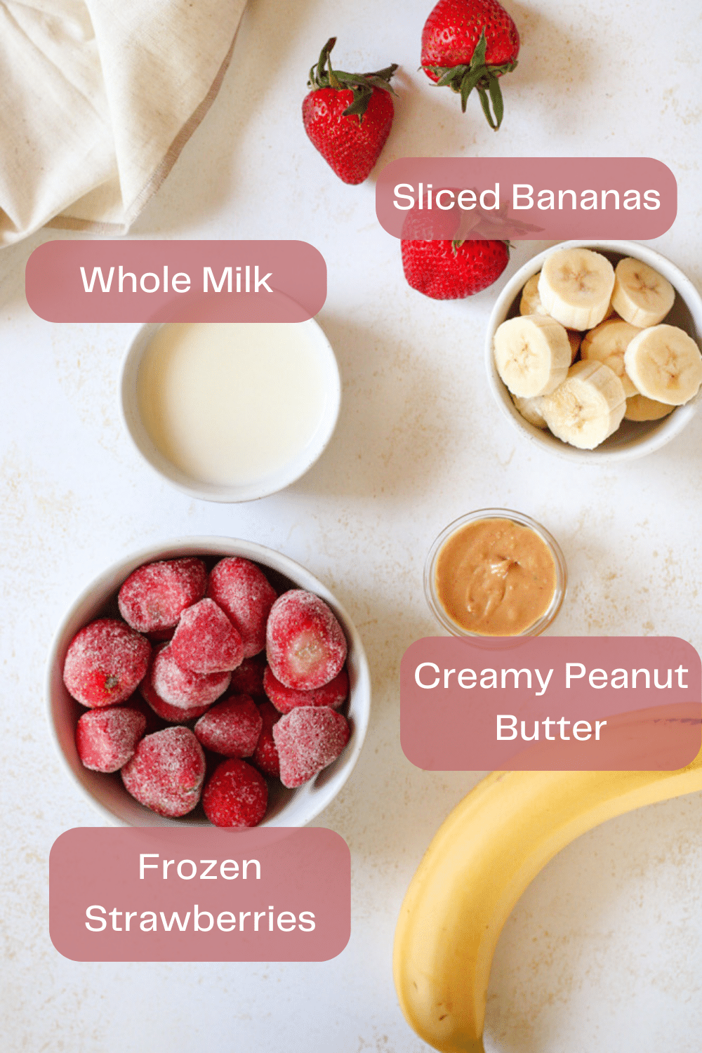 Overhead image of strawberry banana peanut butter smoothie ingredients on table.