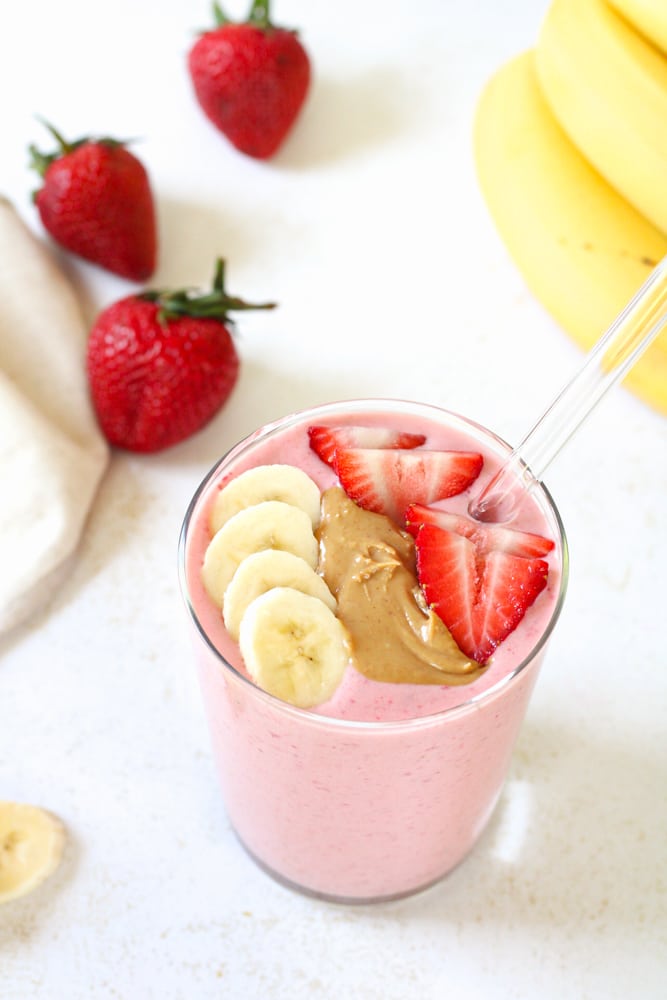 3/4 image of strawberry peanut butter banana smoothie with toppings in a glass. 