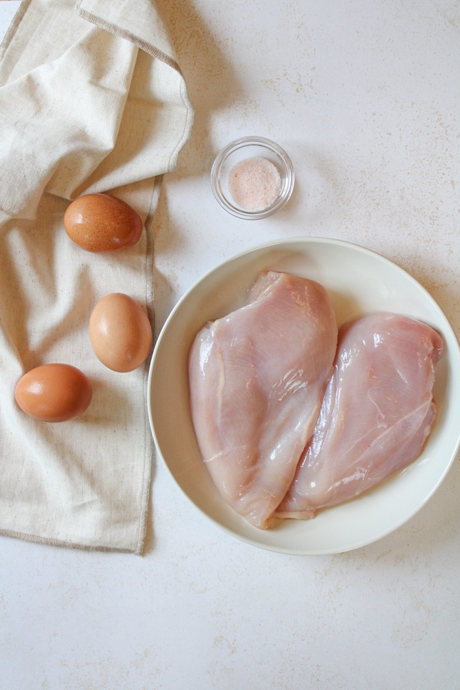 Chicken breasts on a plate with eggs and salt near by.