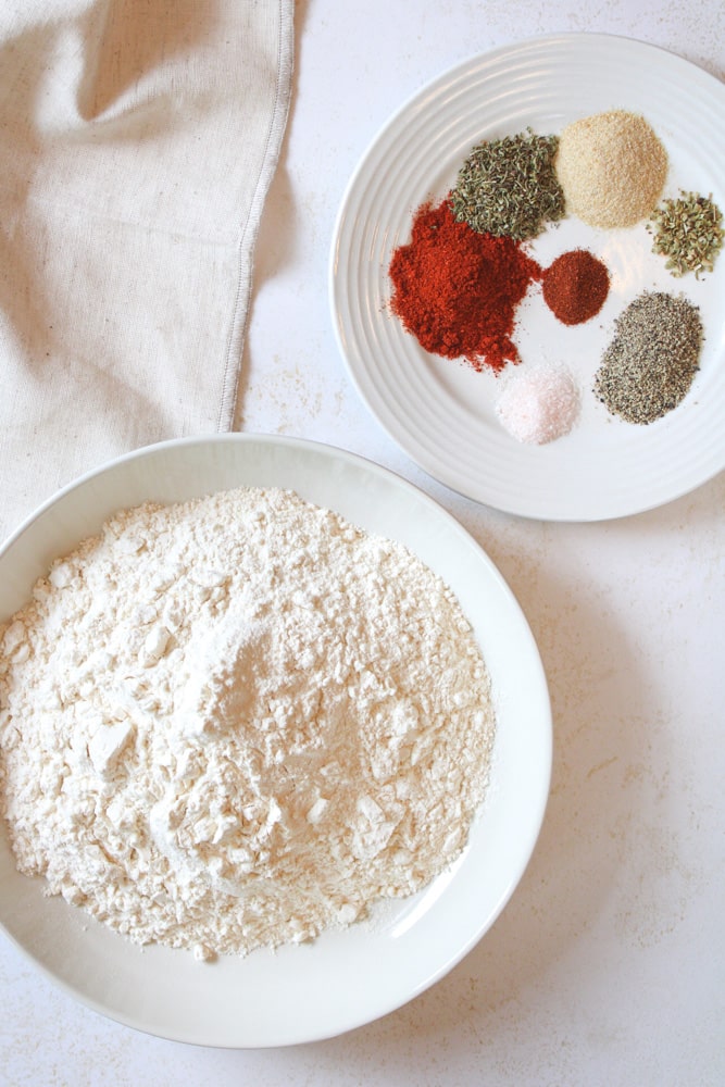 Overhead image of flour in a bowl and a plate of seasonings near by.