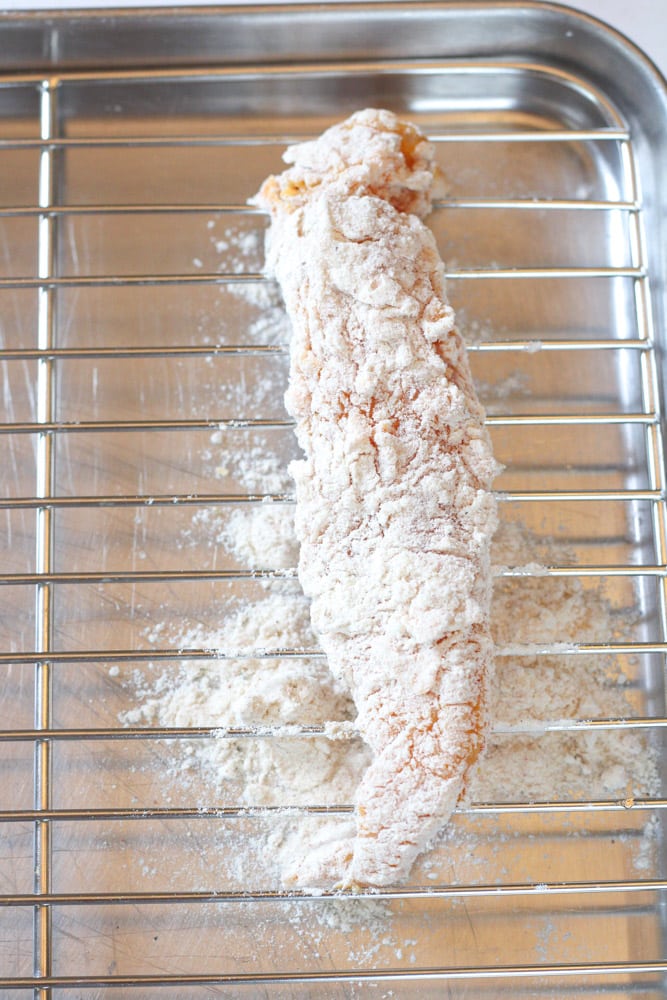 Overhead image of chicken drenched with egg and flour on a wire rack.