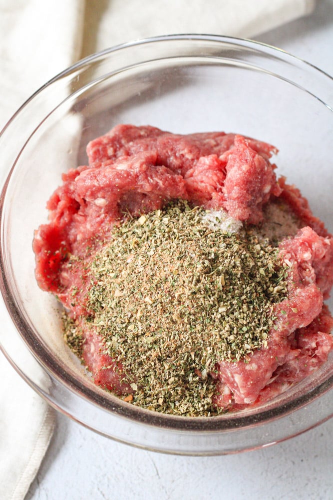 Ground lamb in a bowl with sausage seasoning on top.