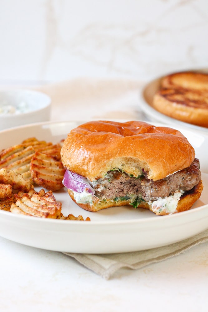Burger with a bite taken out of it on a plate with fries.