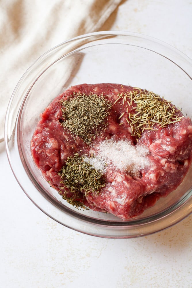 Ground lamb in a bowl with seasonings on top.