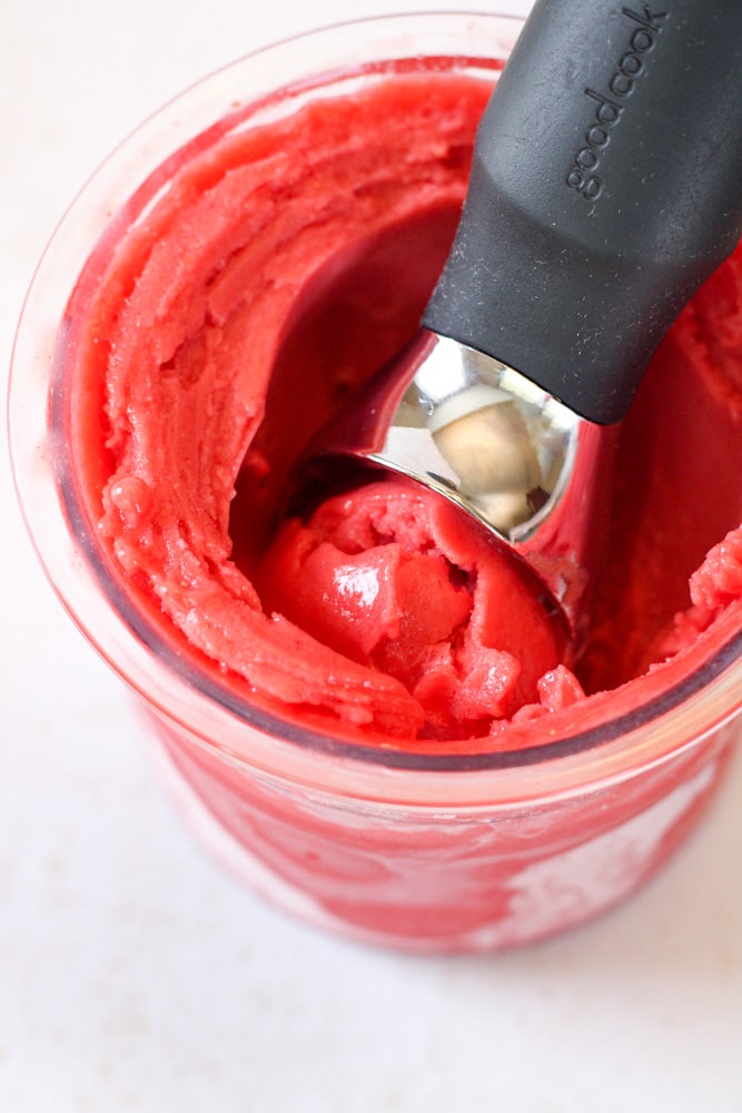 Scoop of sorbet in a container with an ice cream scoop inside.