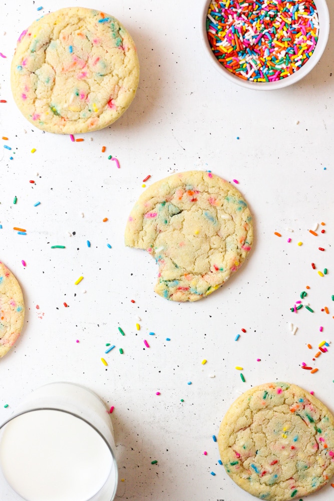 Sugar cookie with a bite missing on a table with sprinkles.