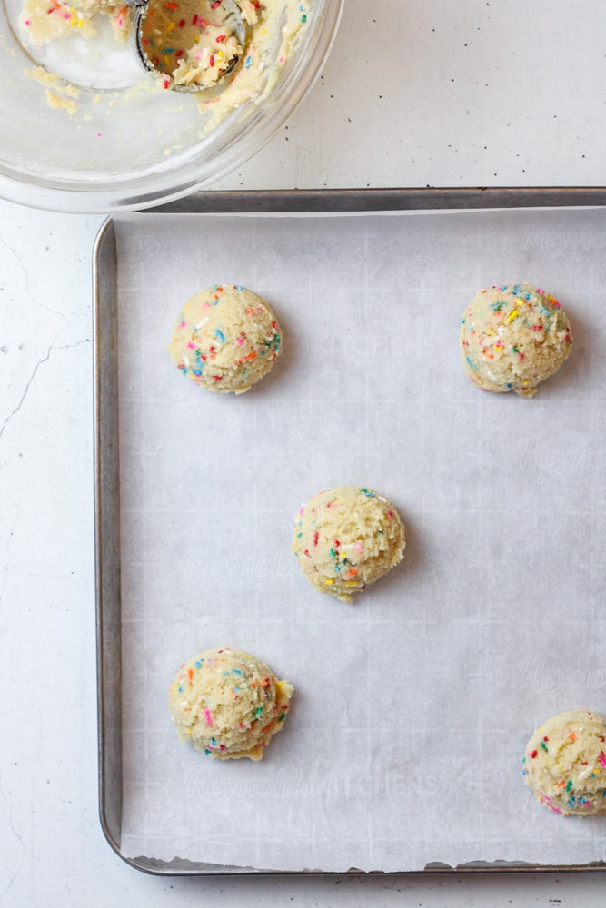 Cookie dough balls on a parchment paper lined sheet pan.