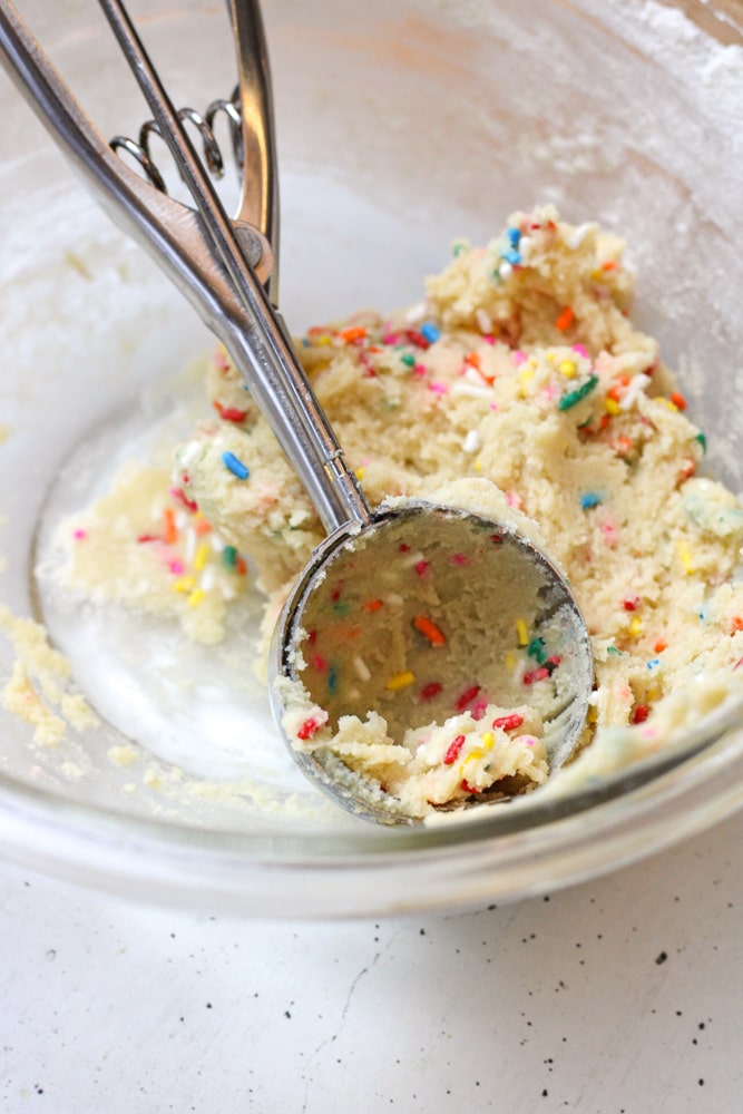 Sprinkle sugar cookie dough in a cookie scoop in a bowl.