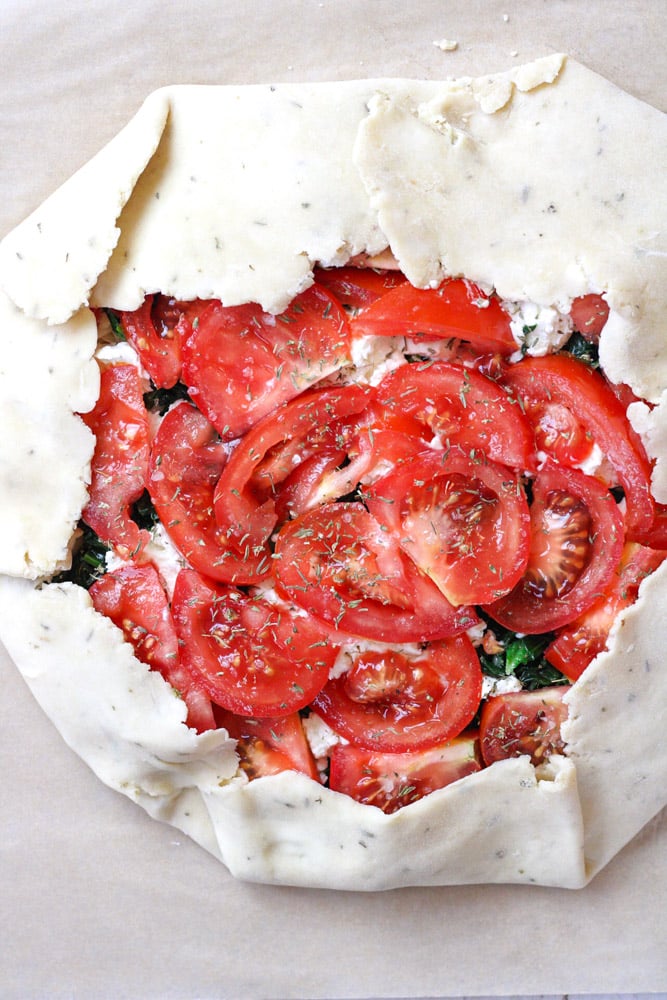 Overhead image of an uncooked tomato galette with the sides folded over.