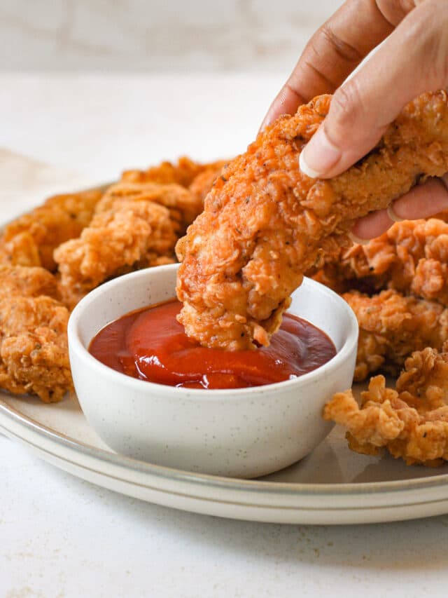 Woman's hand dipping chicken tender into ketchup.