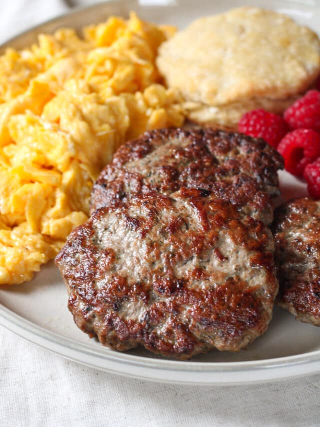 Close up image of breakfast sausage patties on a plate with fruit, eggs, and biscuits.