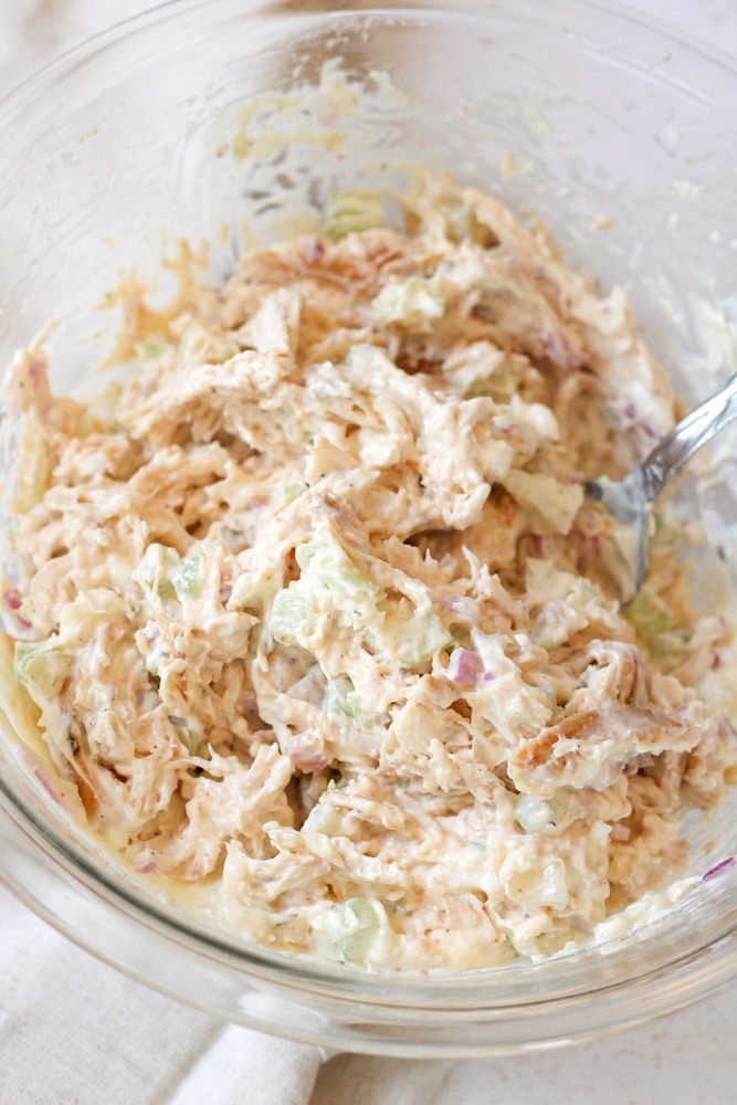 Close up image of chicken salad in a mixing bowl with a spoon.