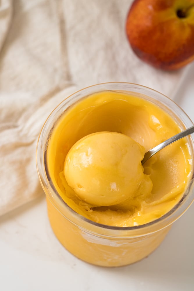 Scoop of peach sorbet in a container with a spoon.