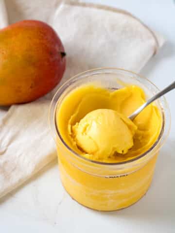 A scoop of mango sorbet with a scoop in a container.