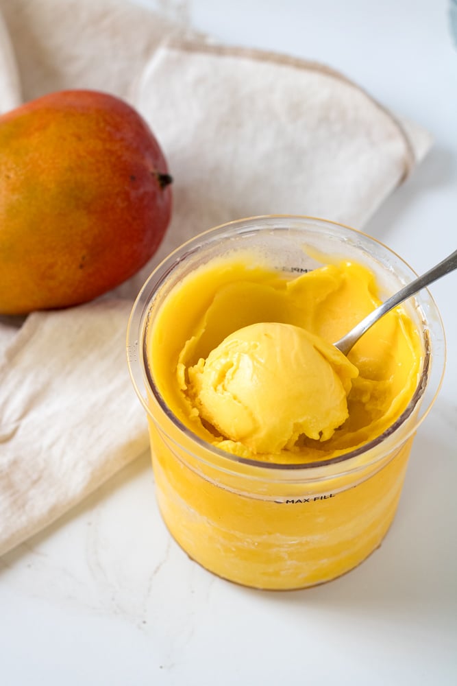 A scoop of mango sorbet with a scoop in a container.