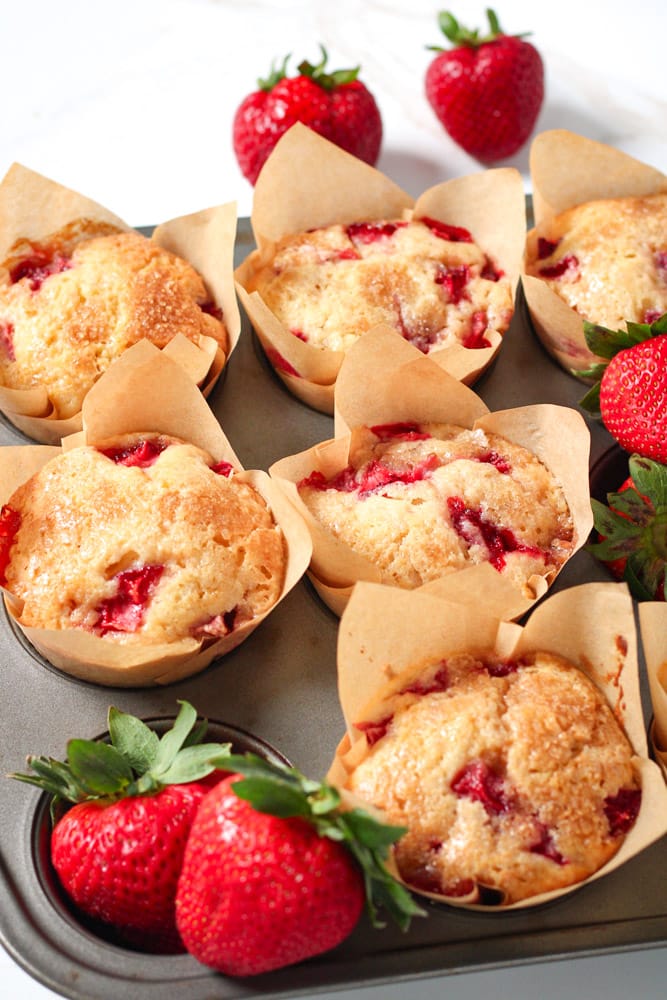 Muffins in a baking pan with fresh strawberries.