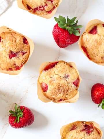 Overhead image of strawberry muffins on a table with fresh strawberries.