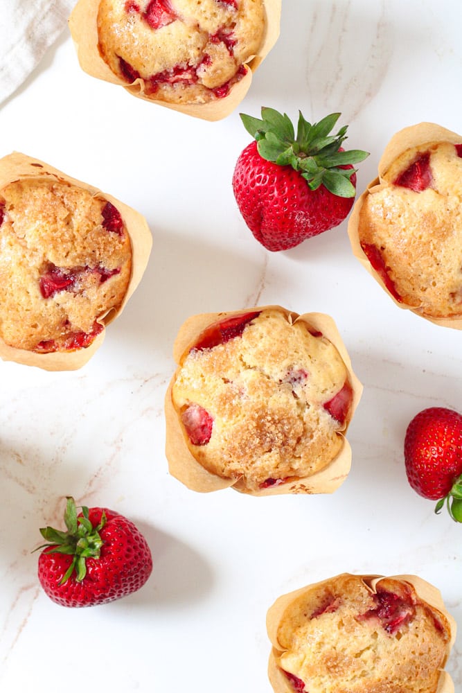 Overhead image of strawberry muffins on a table with fresh strawberries.