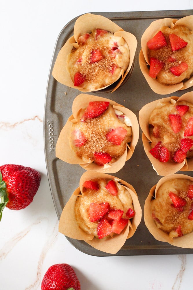 Muffin batter in muffin liners topped with chopped strawberries and turbinado sugar.