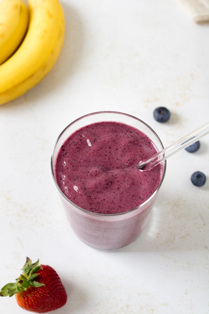 Overhead image of blueberry banana smoothie in a glass with straw.