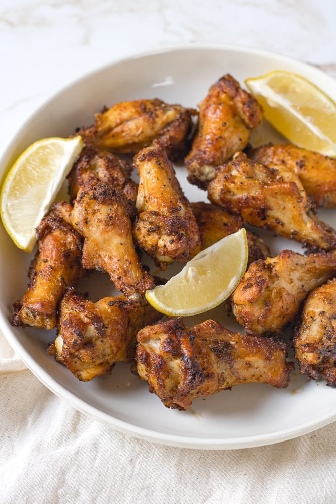 Lemon pepper wings on a plate with lemons.